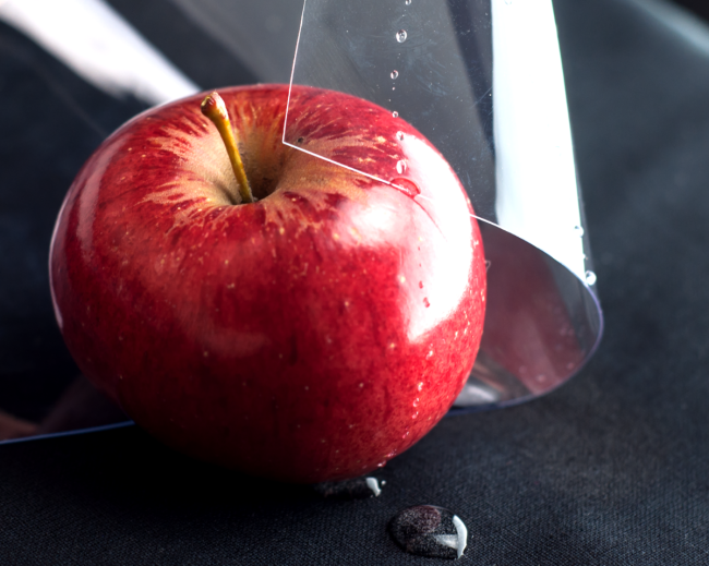 A glossy, transparent sheet of PVC vinyl partially covering a red apple with water droplets on its surface, demonstrating its food-safe properties.