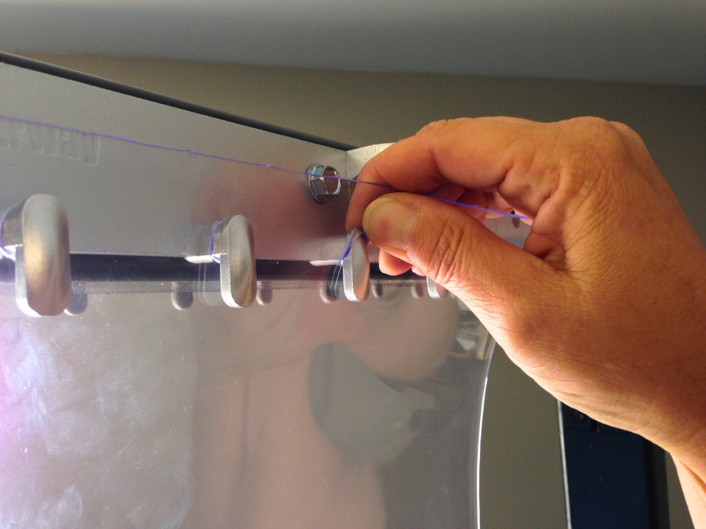 Hand securing clear pvc strip curtain onto metal hanging hooks.