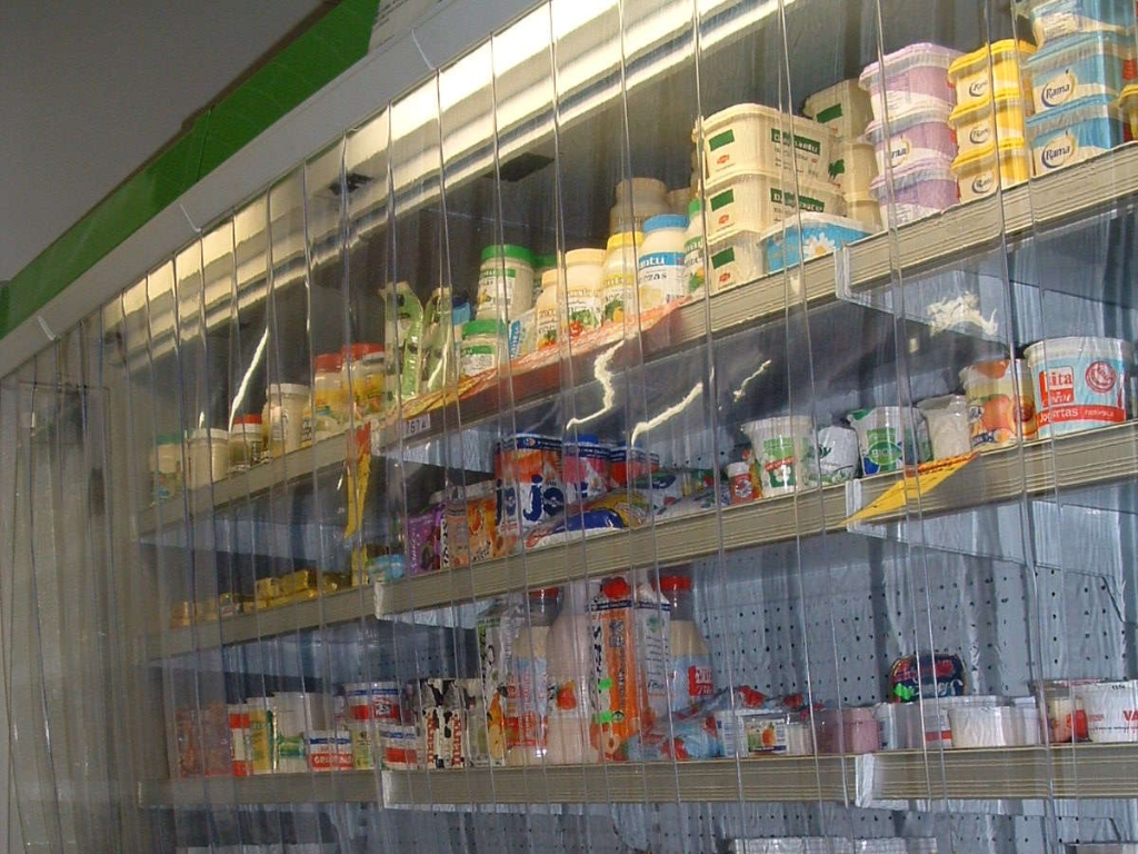 Supermarket refrigerator stocked with dairy products behind clear pvc strip curtains.