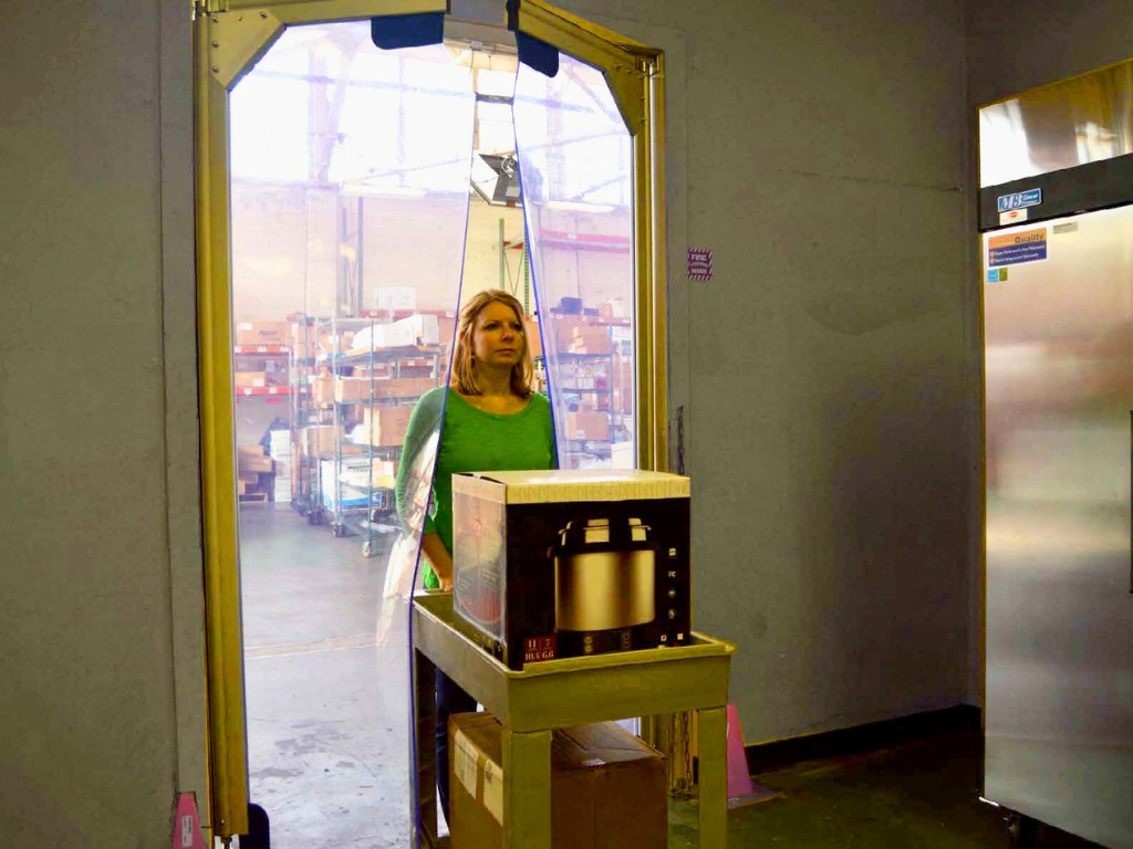 Worker pushing cart with boxes through clear swing pvc doors in warehouse.  File name: worker cart swing pvc doors warehouse.jpg