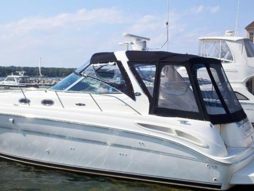 The side of a large white boat with a black canvas enclosure that has clear vinyl windows. Another boat with a similar clear enclosure is visible in the background.