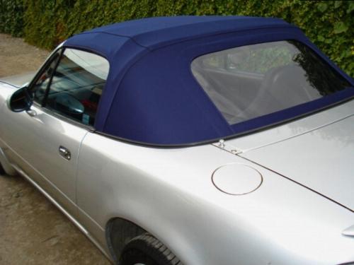 A back and side view of a silver convertible car with a dark blue soft top.