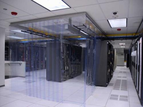  Inside a data center, a large cube-shaped enclosure made of clear plastic strips surrounds a section of server racks.