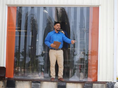 A man points outside a warehouse through a PVC strip curtain.