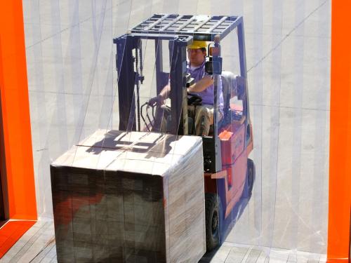 A man on a forklift drives through a PVC strip curtain.