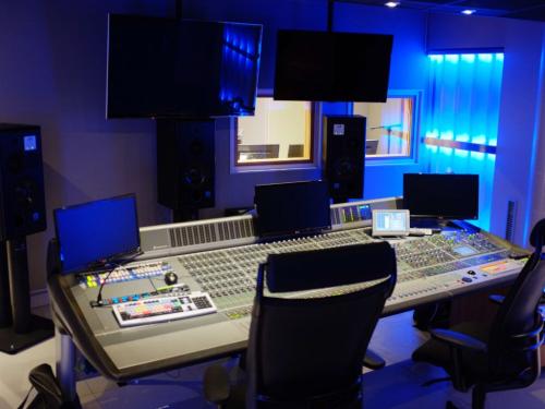 Modern recording studio control room with large mixing console, multiple monitors, and ambient blue lighting.