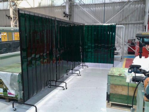Portable welding booths with green strip curtains set up inside workshop.