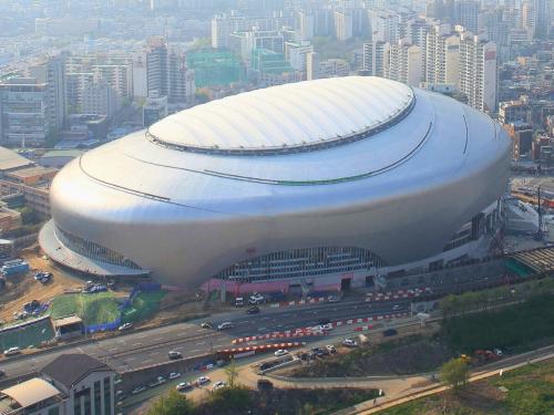 Aerial view of the Seoul Sky Dome, a large silver-domed sports and concert arena surrounded by city buildings.