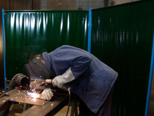 Welder at work with sparks flying inside green welding screen booth.