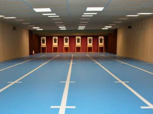 Wide indoor shooting range with blue lanes and silhouette targets at the end.